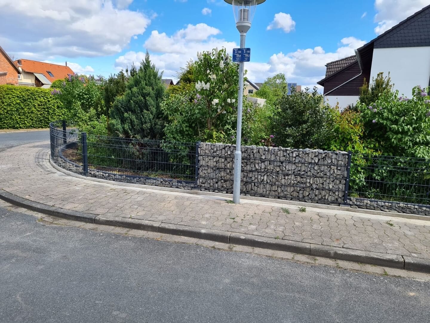 Der Blick von der Straße auf einen Zaun mit abwechselnden Stein- und Drahtelementen